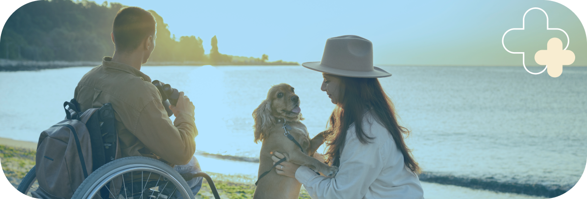 A man in a wheelchair, a woman and a dog enjoying time at the waterfront, demonstrating the importance of connection in mental health support for people with physical disabilities. 