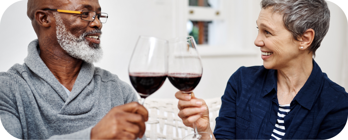 Two older Australians smile while sharing wine and enjoying activities for seniors in Perth, such as wine tastings in Swan Valley.