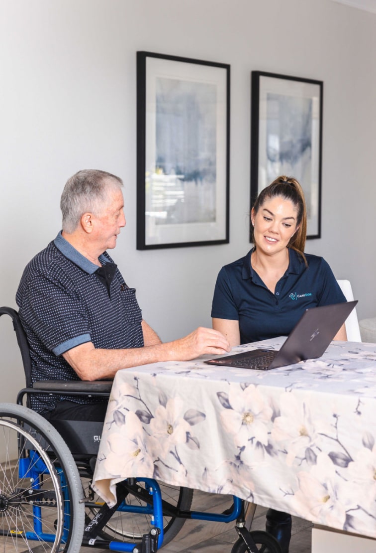 A photo of a support worker and a home care recipient looking at a computer and reviewing aged care services in Canberra.