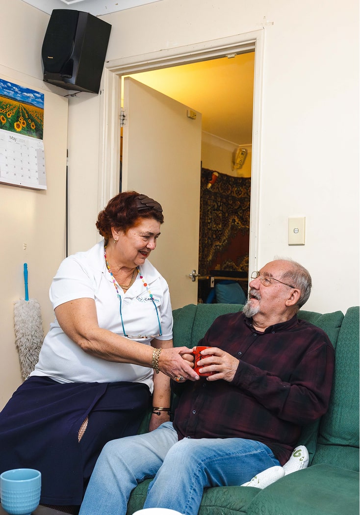 A photo of home care in Townsville, with a support worker handing a man a cup of tea.