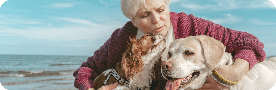 A photo of a woman enjoying the health benefits of pets while visiting the beach with her dogs.