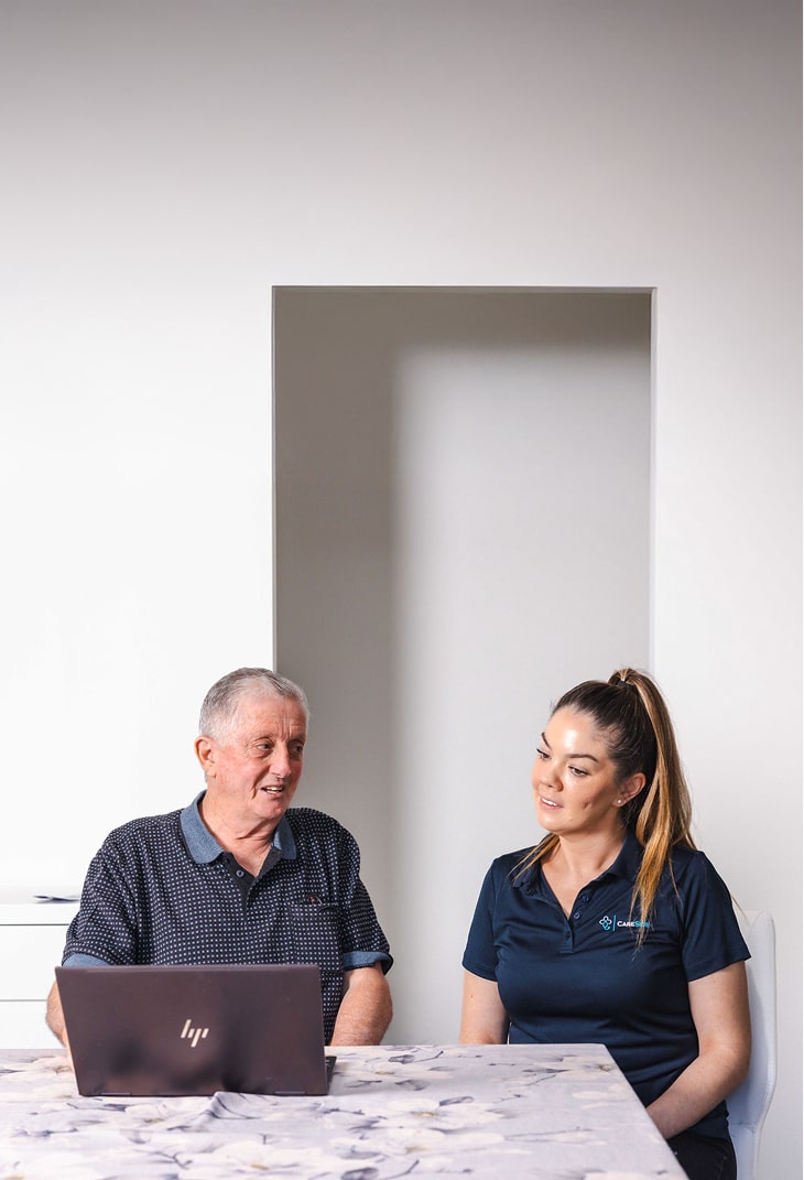 A photo of home care in Cairns shows a man sitting at a table discussing his support services with his caregiver.