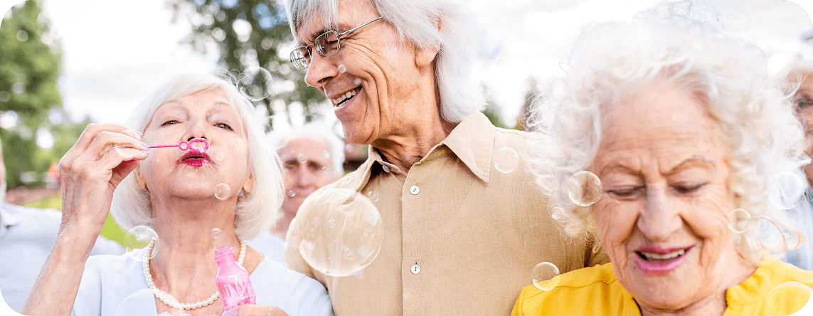 A photo of older people ageing joyfully while laughing and blowing bubbles.
