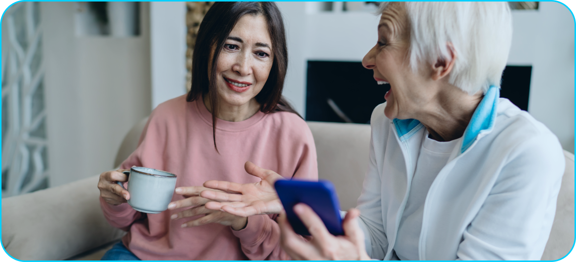 An image of two people laughing and using a cellphone while implementing tips they learned in this AI guide for seniors.